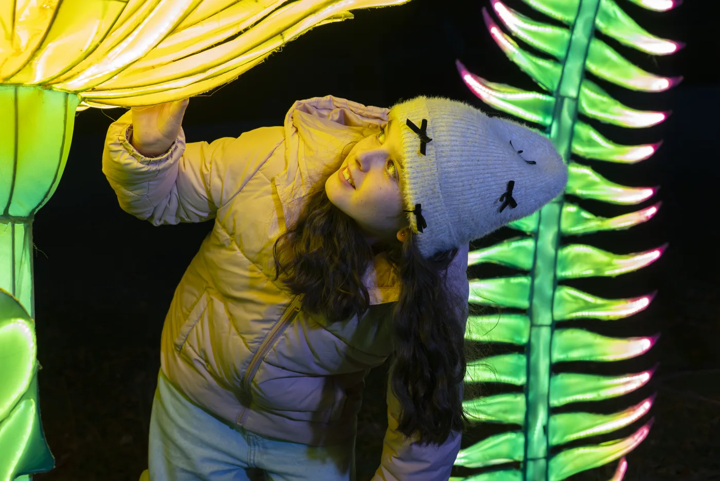 A child under a large glowing flower lantern beside a lit fern